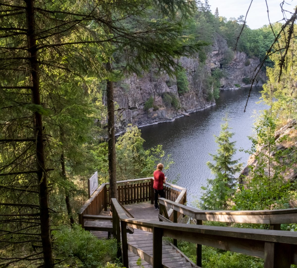 Person står på plattform med utsikt över sjö. Foto.