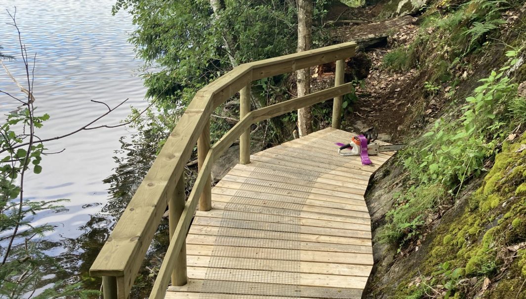 Spång med en bergsvägg på ena sidan och en sjö på andra. Foto.