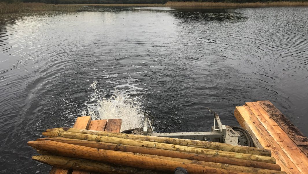 Maskin i sjö som är lastad med brädor och stolpar. Foto.