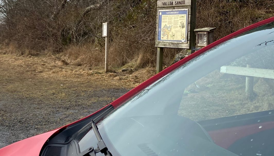 Bil i förgrunden och en skylt om Vallda naturreservat i balgrunden. Foto.