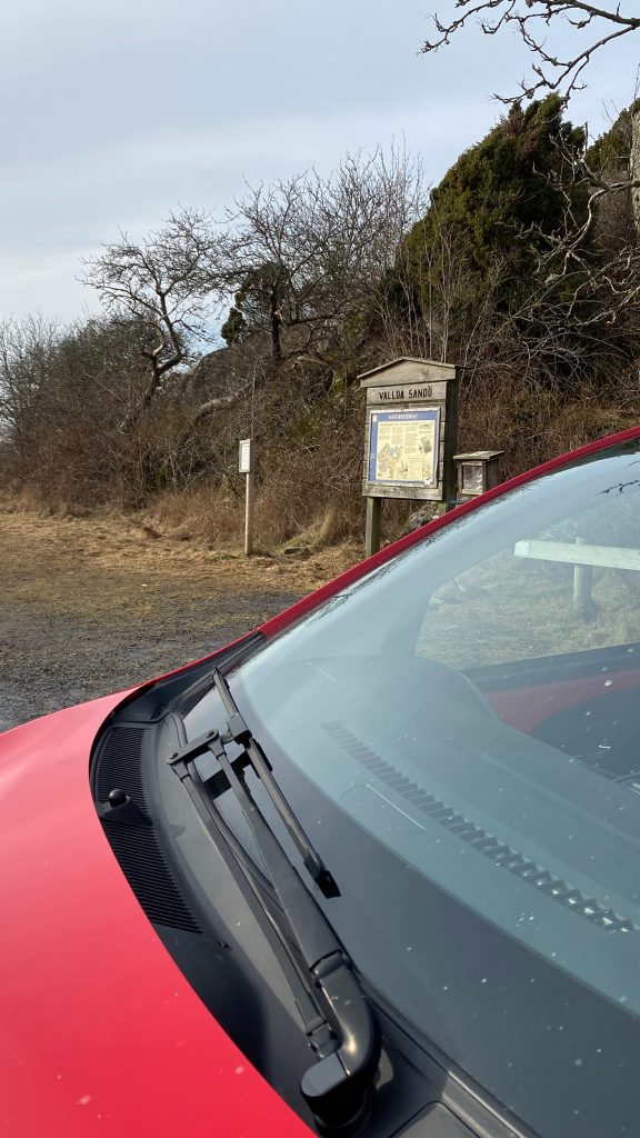 Bil i förgrunden och en skylt om Vallda naturreservat i balgrunden. Foto.