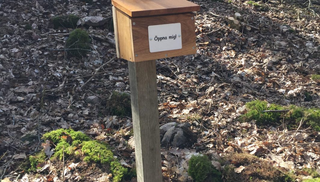 En låda med texten "öpnna mig2 på en stolpe i skogen. Foto.