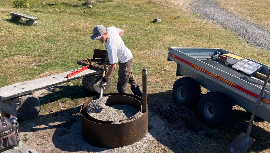 En persion iordningställer en eldstad; skyfflar grus. Foto.