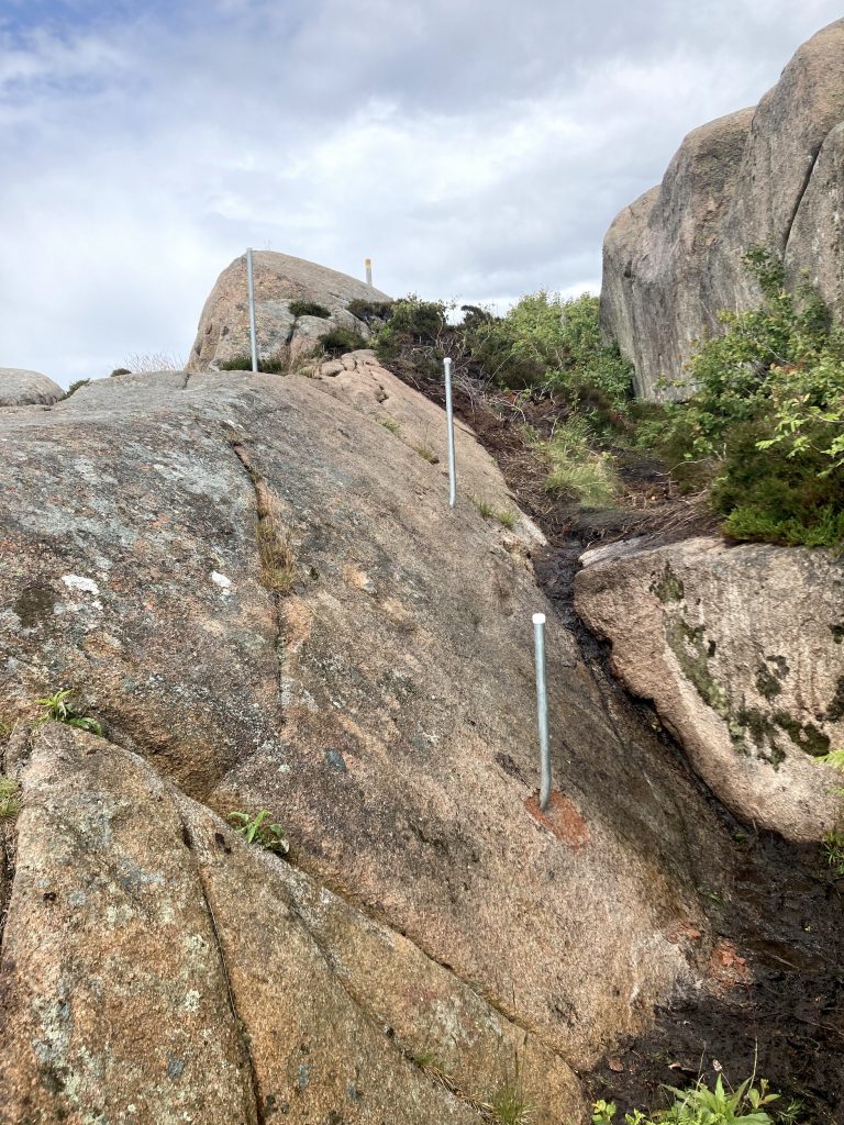 En passage i ett klippområde, med stolpar i metall. Foto.