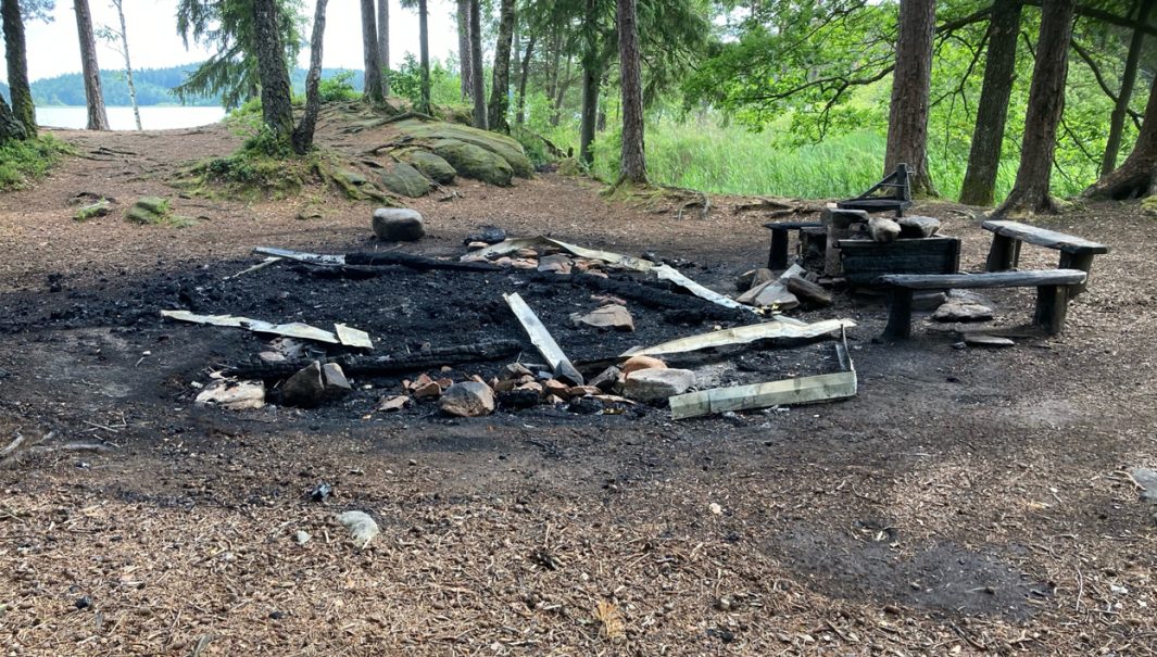Nedbrunnet vindskydd i skogen vid en sjö.Foto.
