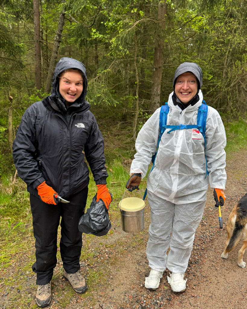 Två glada personer i regn med pensel och sekatör. Foto.