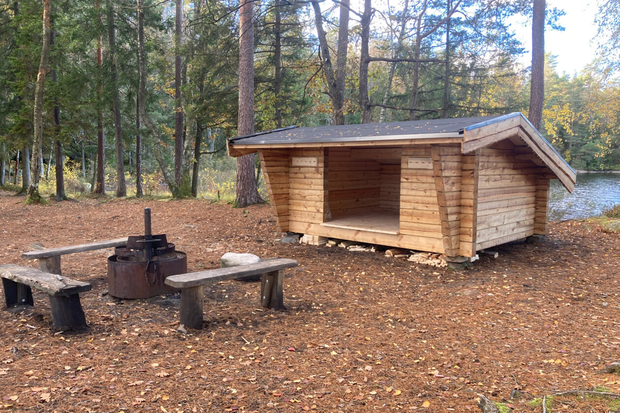ett timrat vindskydd med en eldstad och bänkar framför. Foto.