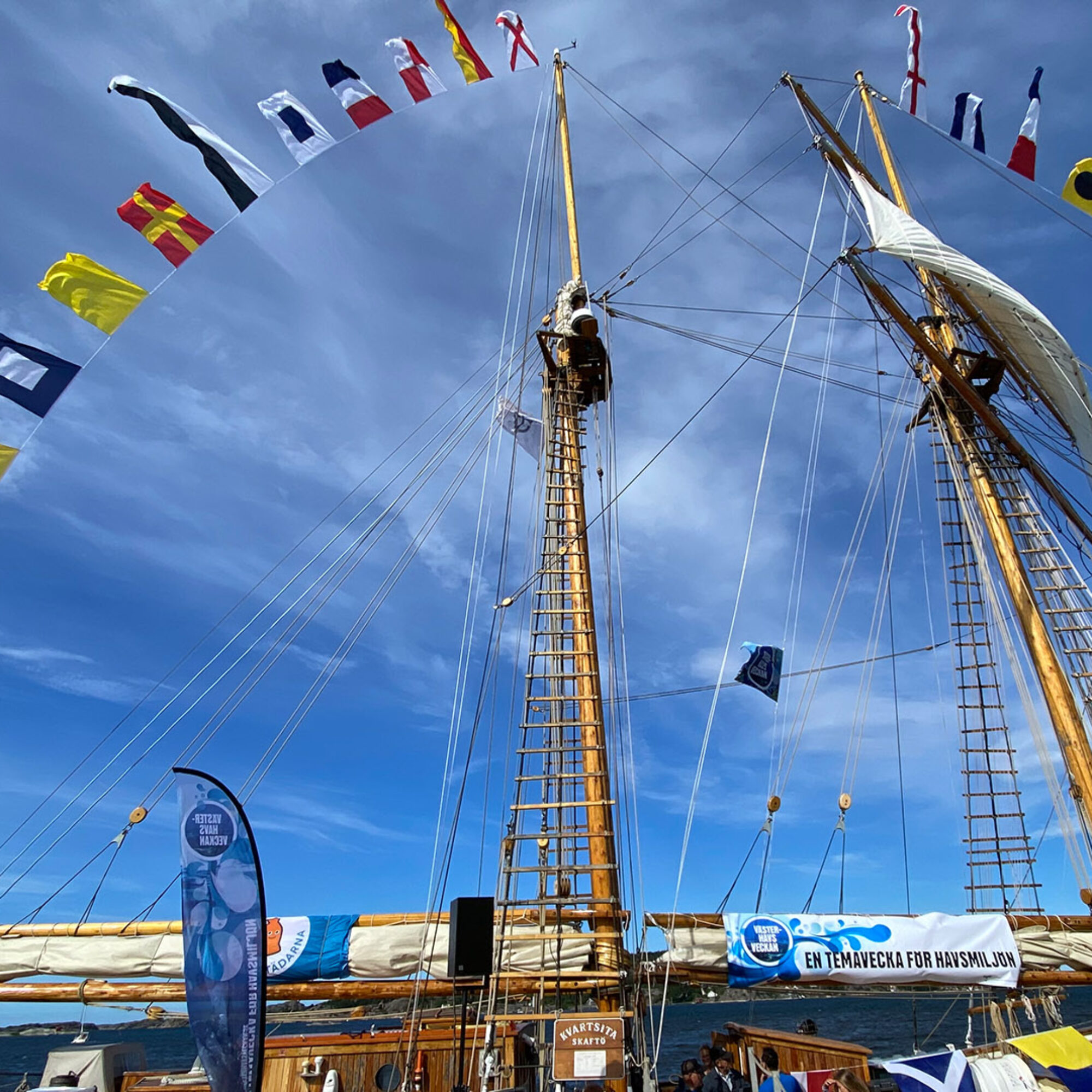 Foto av toppsegelskonaren Kvartsitas två master med flaggspel. Blå himmel med lätta molnskyar i bakgrunden.