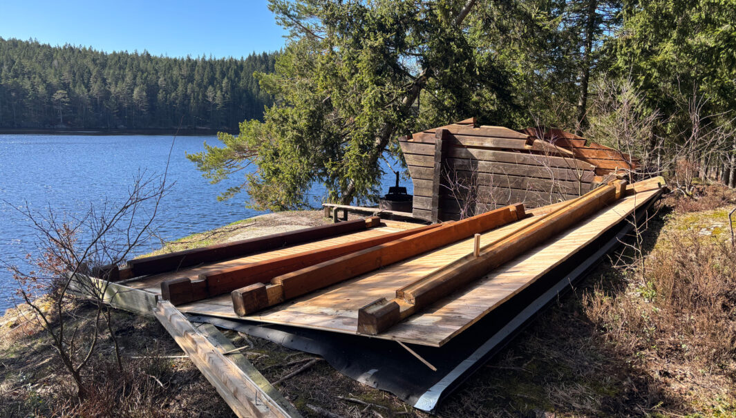 Vindkydd med bortblåst tak som ligger på marken i förgrunden. Foto.