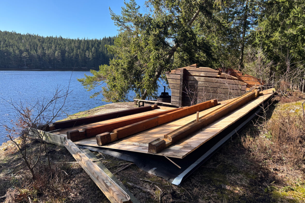 Vindkydd med bortblåst tak som ligger på marken i förgrunden. Foto.