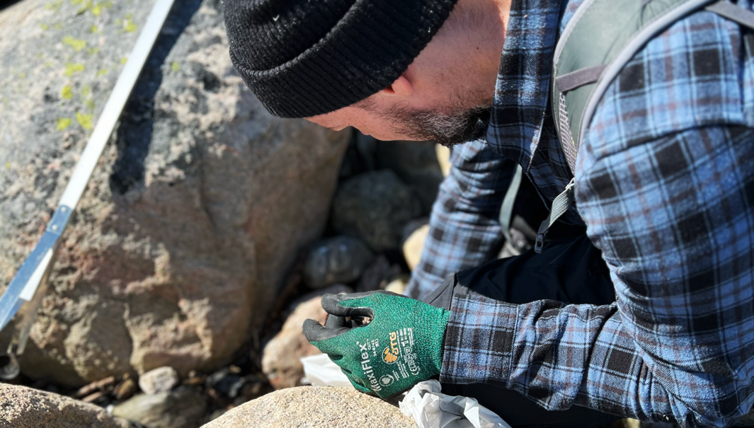 En person som strandstädar på västkusten bland granitklippor.