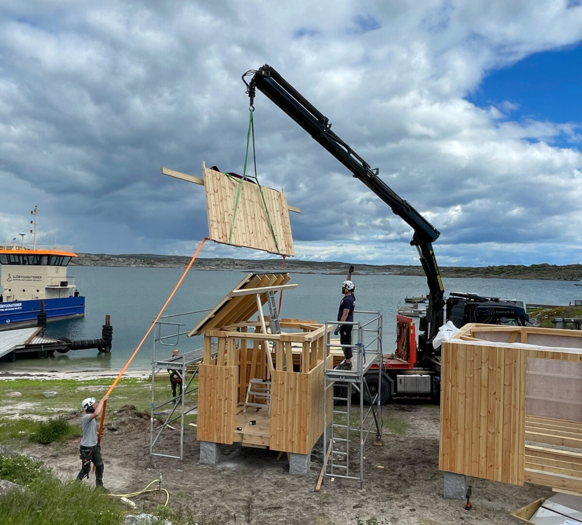 Kranbil lyfter ena halvan av ett sadeltag. Foto.